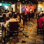 The main floor of the Flying Iguana Taqueria during service. Live music is playing at the back of the room. Patchwork cement tile is used on the floor, and on the wall behind the bandstand.