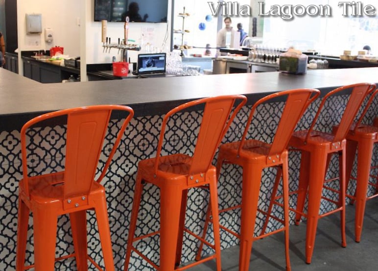 Counter front covered in our blue and white Breeze cement tile with bright Orange chairs in front.