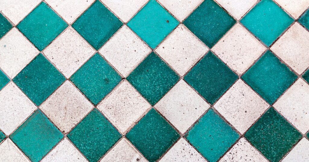 A wall space is meticulously tiled with white and teal square tiles in a checkerboard pattern. It is lightly dirty.