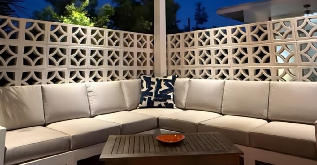 A corner of a couch is bumped up against a wall of breeze blocks. It is an outdoor environment, and it is night.