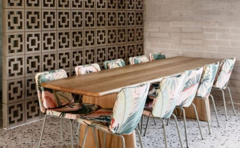 A table with chairs around it is next to a wall of breeze blocks. The floor is made of tile, and the wall is brick.