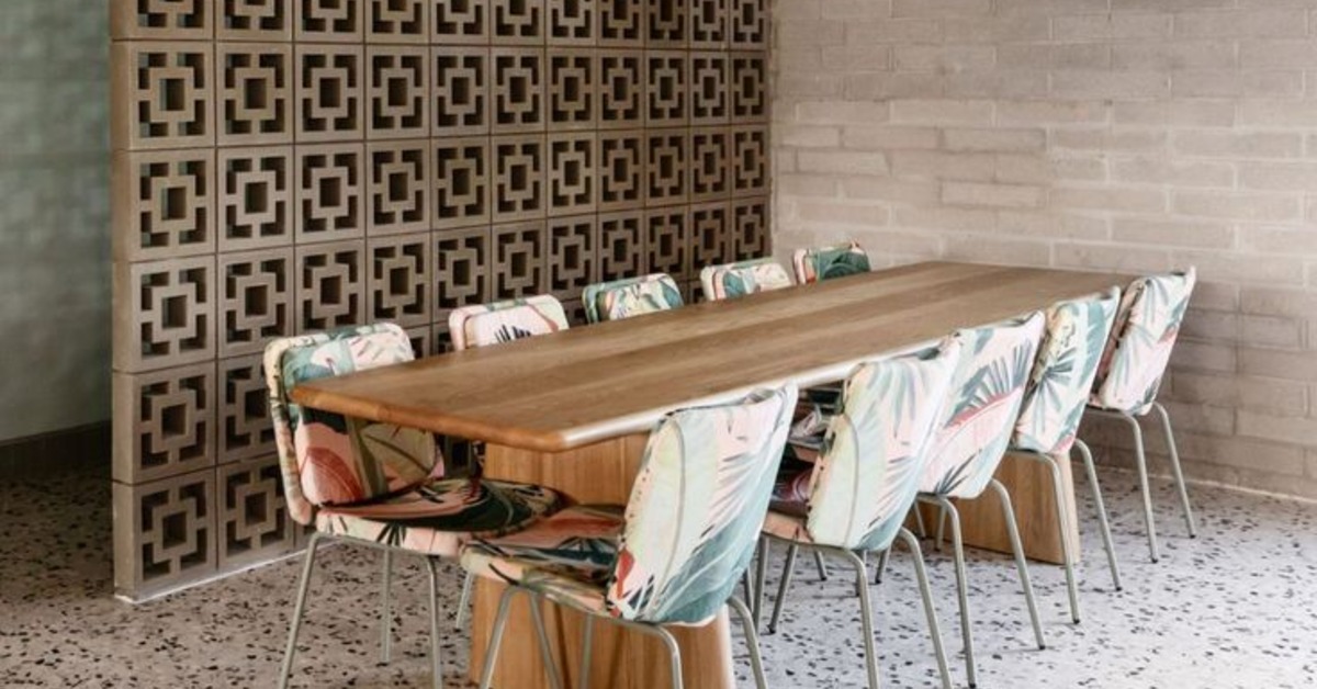 A table with chairs around it is next to a wall of breeze blocks. The floor is made of tile, and the wall is brick.