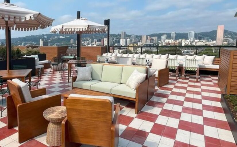 Outdoor furniture, such as chairs and couches, are on a red and white tile patio. There is a city in the background.