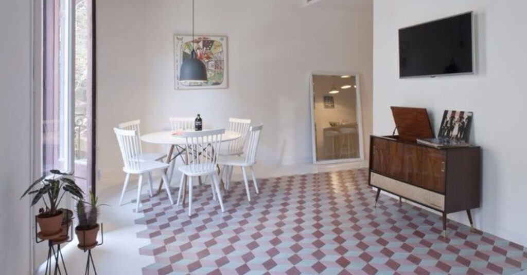 A room with a table and several chairs surrounding it. There is tile on the floor and the walls are white.