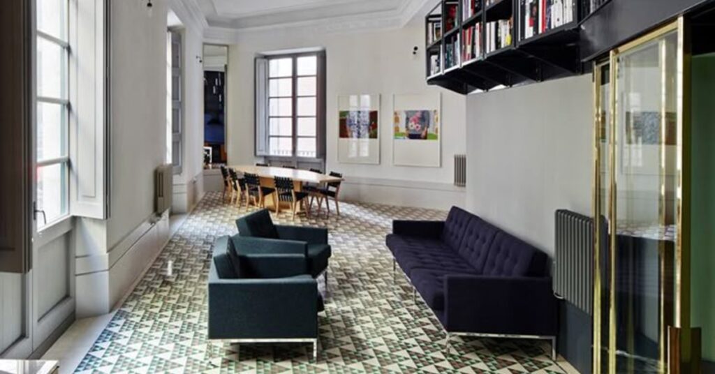 A black couch faces two black chairs in the middle of a room. There are windows along the white walls.