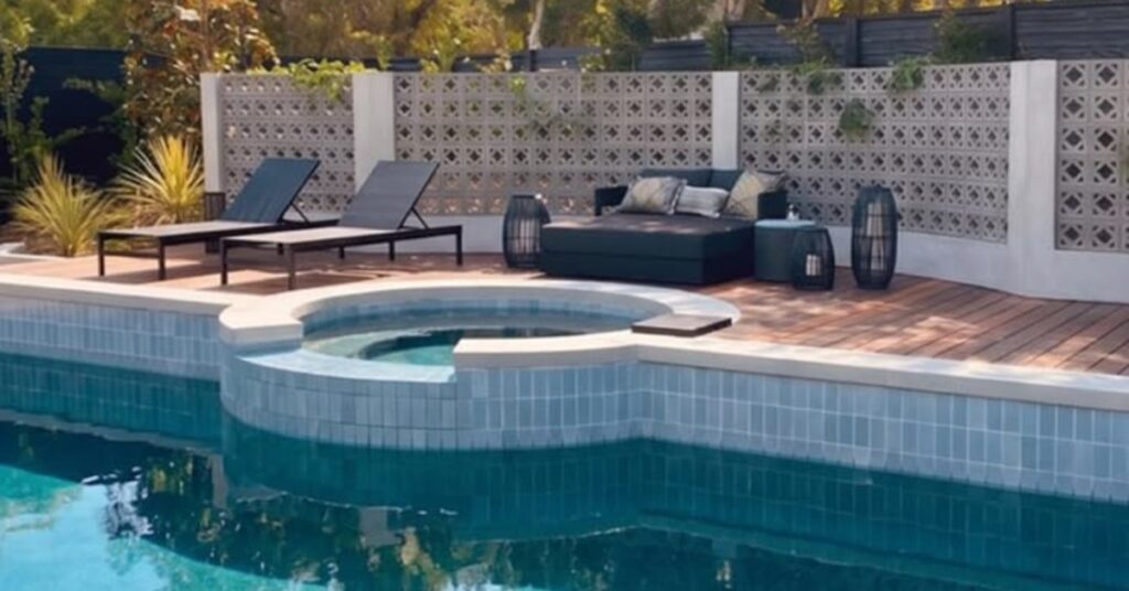 Several pieces of outdoor furniture are placed around a circular hot tub. There is a wall of blocks behind the furniture.