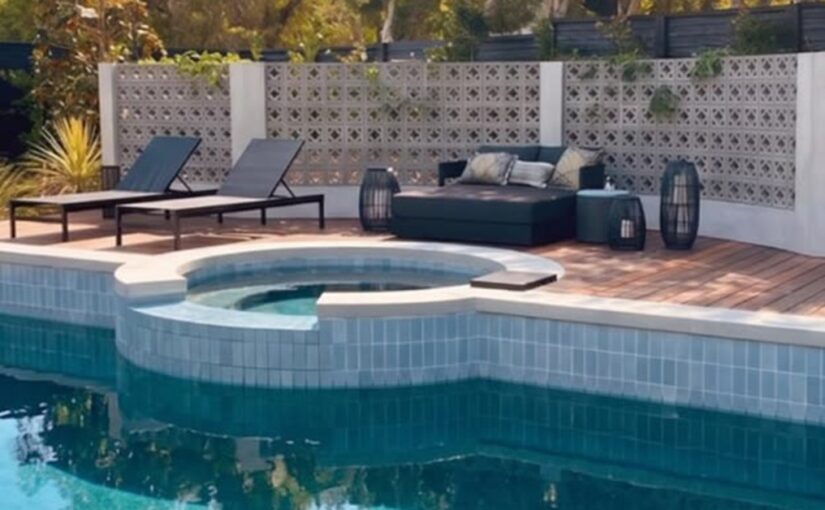 Several pieces of outdoor furniture are placed around a circular hot tub. There is a wall of blocks behind the furniture.