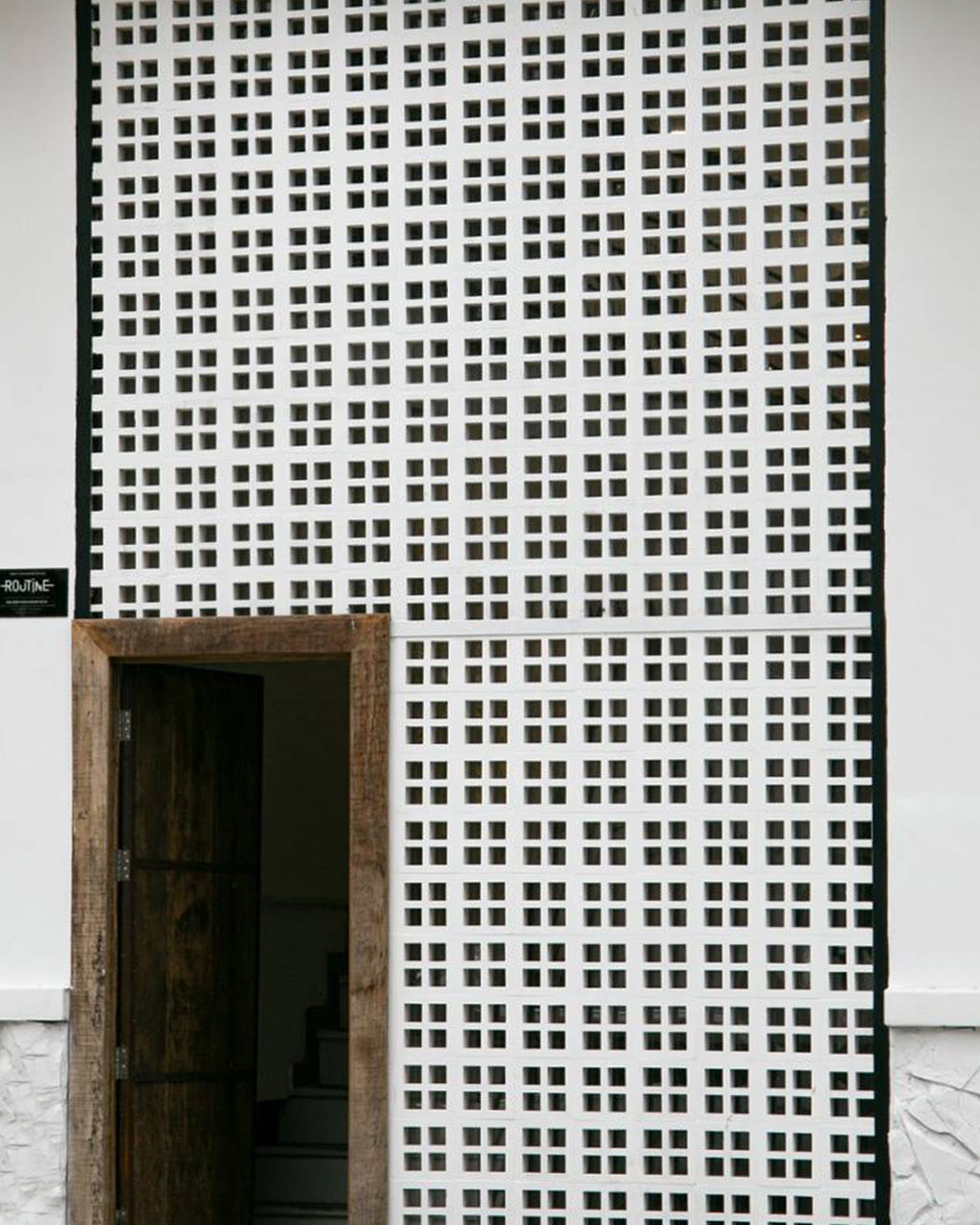 Minimalist Facade: White Geometric Breeze Block Screen with Rustic Wood Door